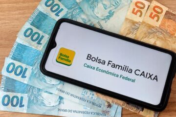 Um celular com notas de 100 e 50 reais embaixo mostrando a logo do Bolsa Família 2023.